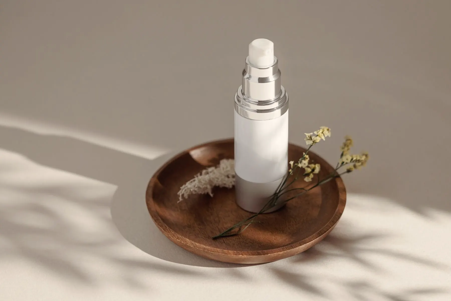 Pump bottle on a wooden dish with dried flowers in soft daylight