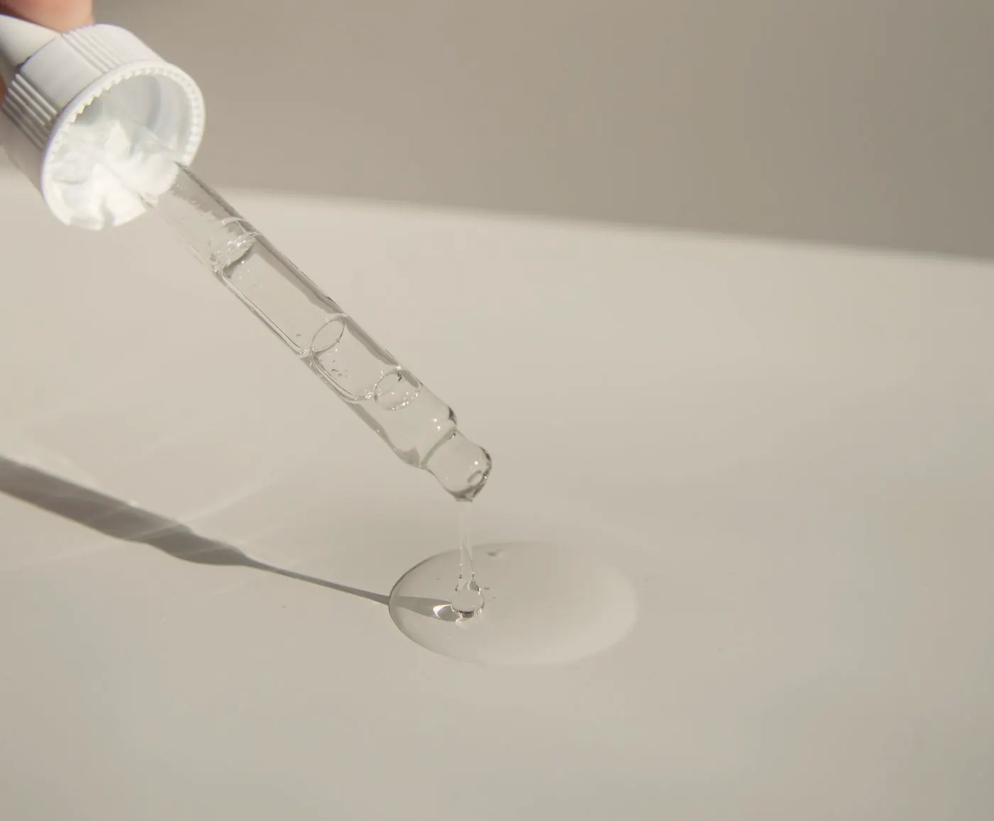 Glass dropper releasing a clear drop of serum